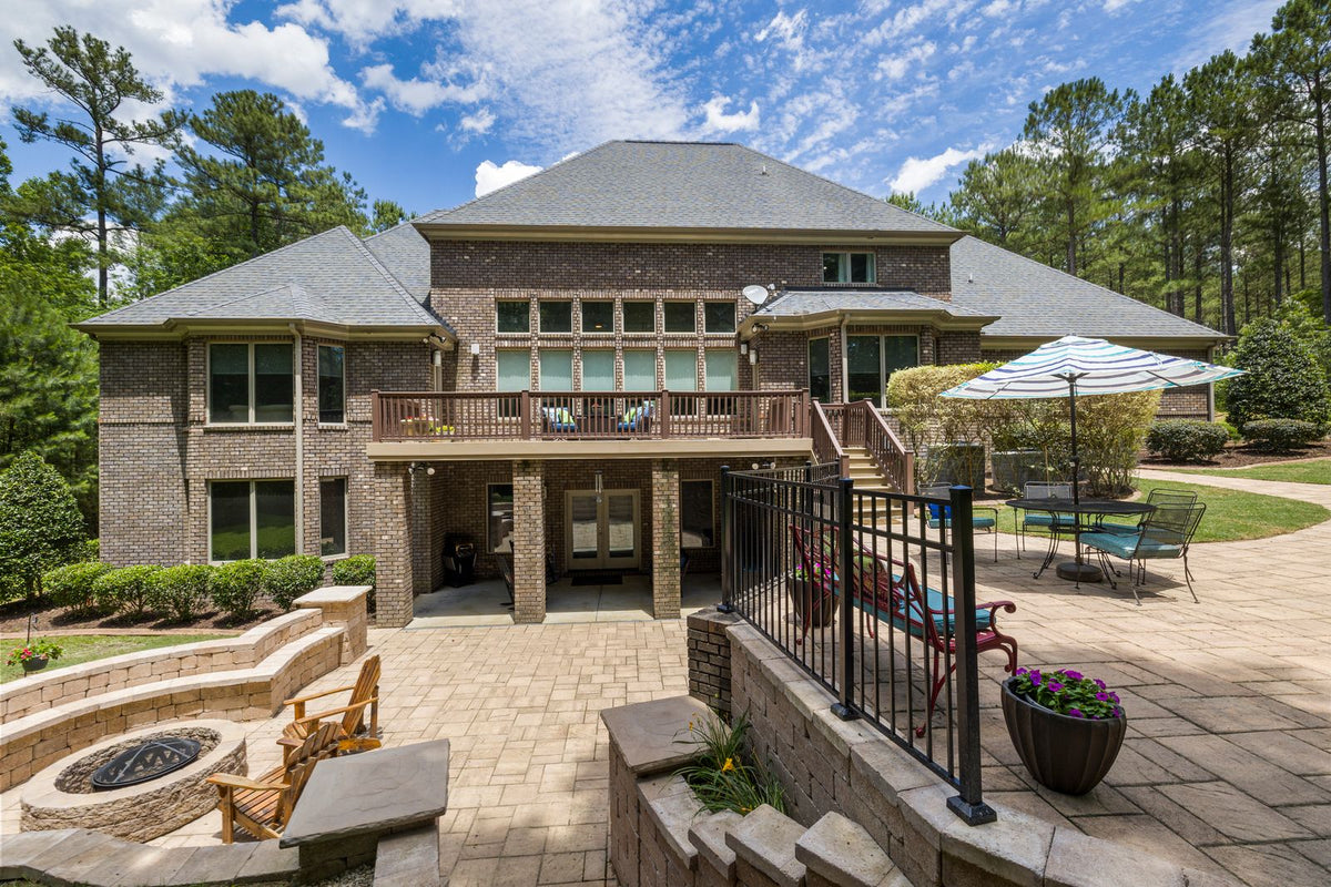 Sunny backyard with a stone patio, built-in fire pit, lounge chairs and an umbrella table