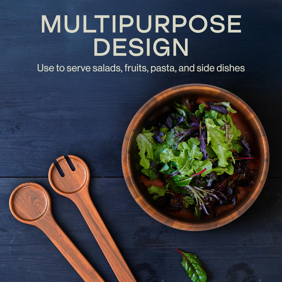 Overhead view of the Laroda acacia salad bowl filled with leafy greens beside the wooden serving fork and spoon on a dark table