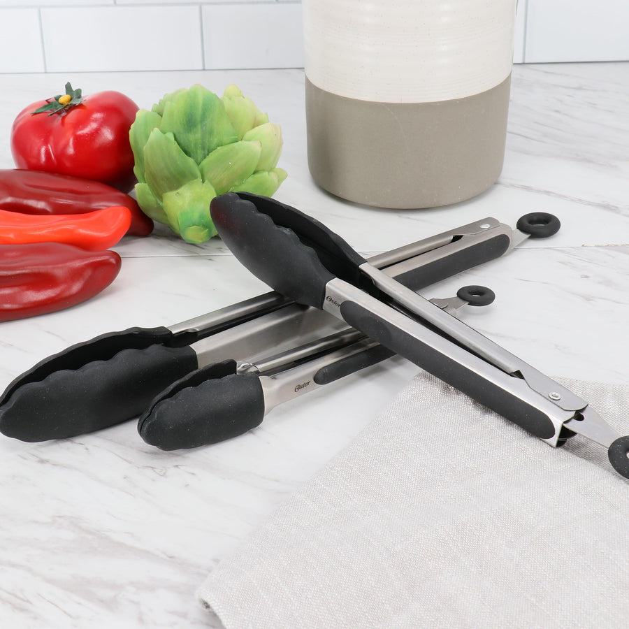 Stainless steel kitchen tongs with black nylon tips beside fresh vegetables