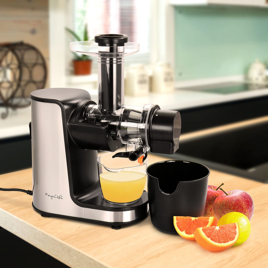 MegaChef masticating slow juicer on a kitchen counter with fresh orange juice in the cup beside apples and oranges
