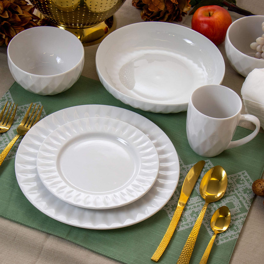 Elama Sienna white porcelain dinnerware place setting on a green placemat with gold flatware and serving bowl