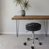 Elama black tufted backless rolling stool at a wood desk with hairpin legs, lifestyle in a home workspace