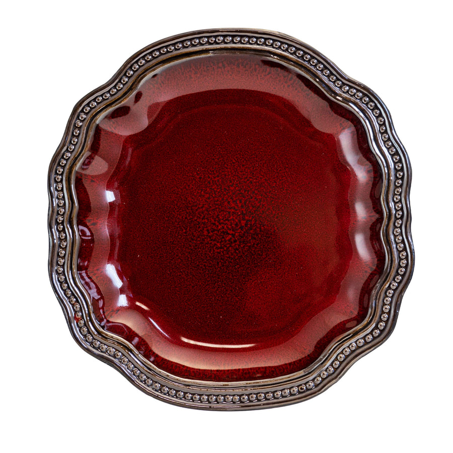Top view of an Elama Regency red stoneware plate with a speckled red glaze center and scalloped beaded gold-tone rim