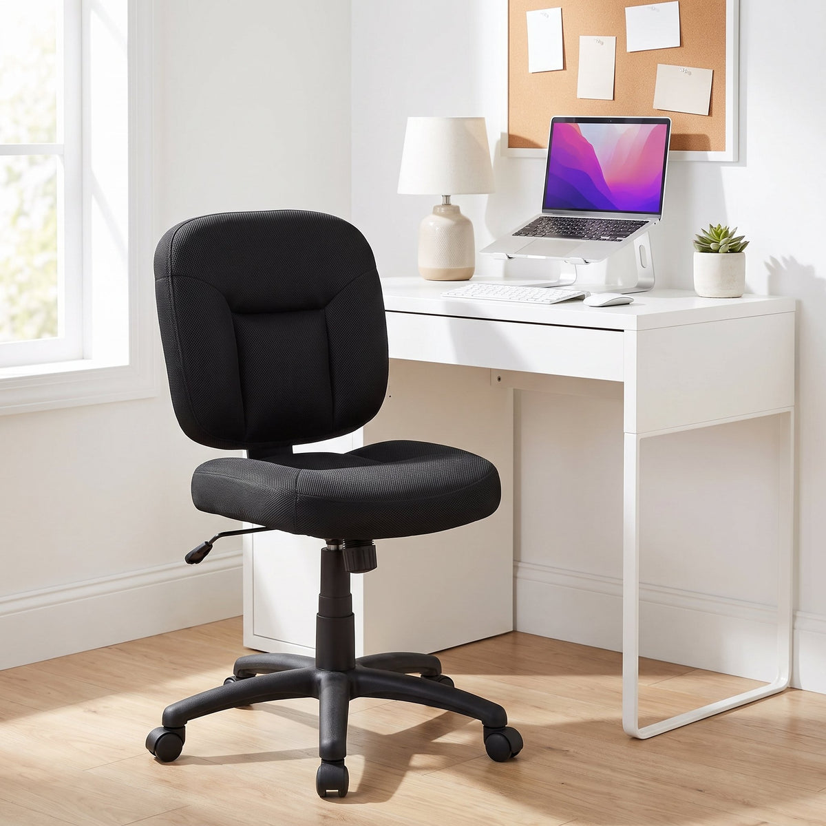 Armless black office task chair at a compact white desk with a laptop stand and lamp in a small home office nook