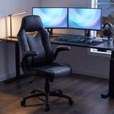 Black and gray ergonomic office chair with flip-up arms at a dual monitor gaming and work desk with keyboard and headset