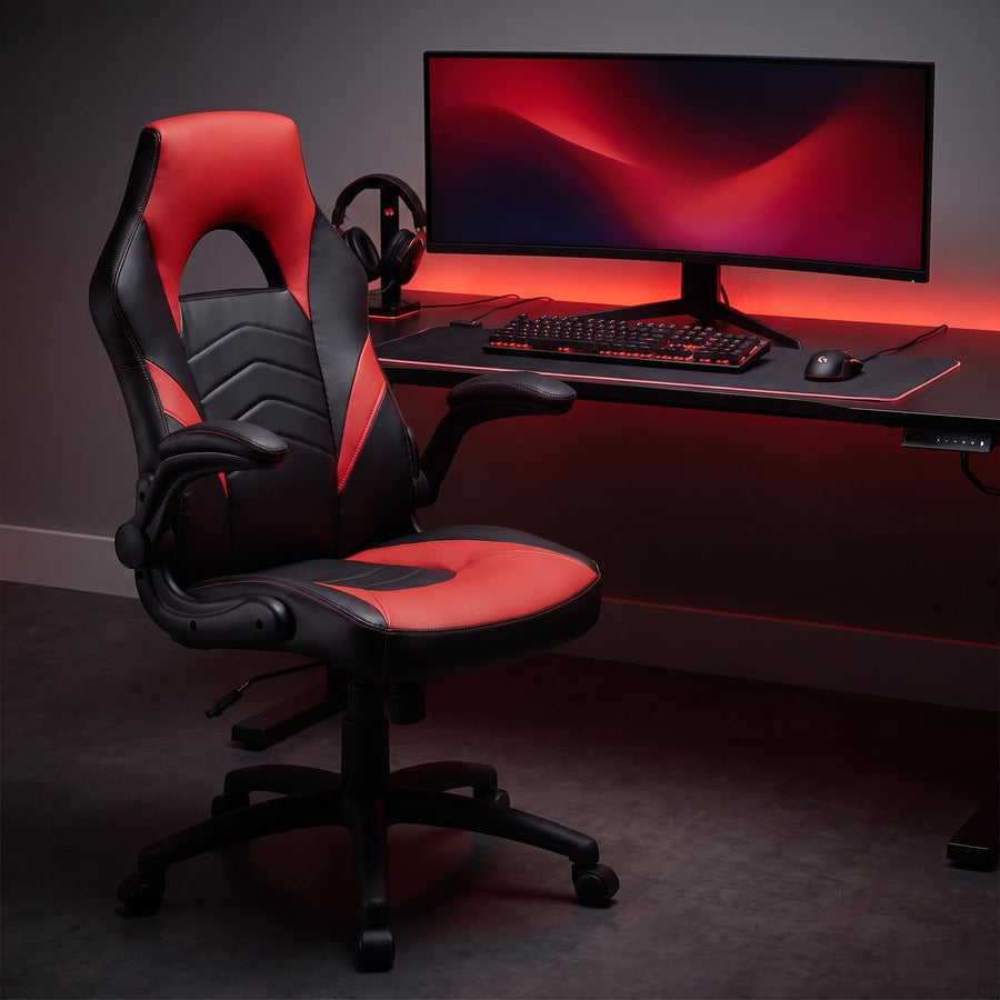 Black and red gaming chair with flip-up arms at a battle station desk with a red-lit keyboard, monitor and headset at night