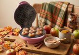 Pink Brentwood TS-250 mini donut maker open with seven fresh apple cider mini donuts, cinnamon sugar, apples, cinnamon sticks, and a mug of hot cider on a fall table