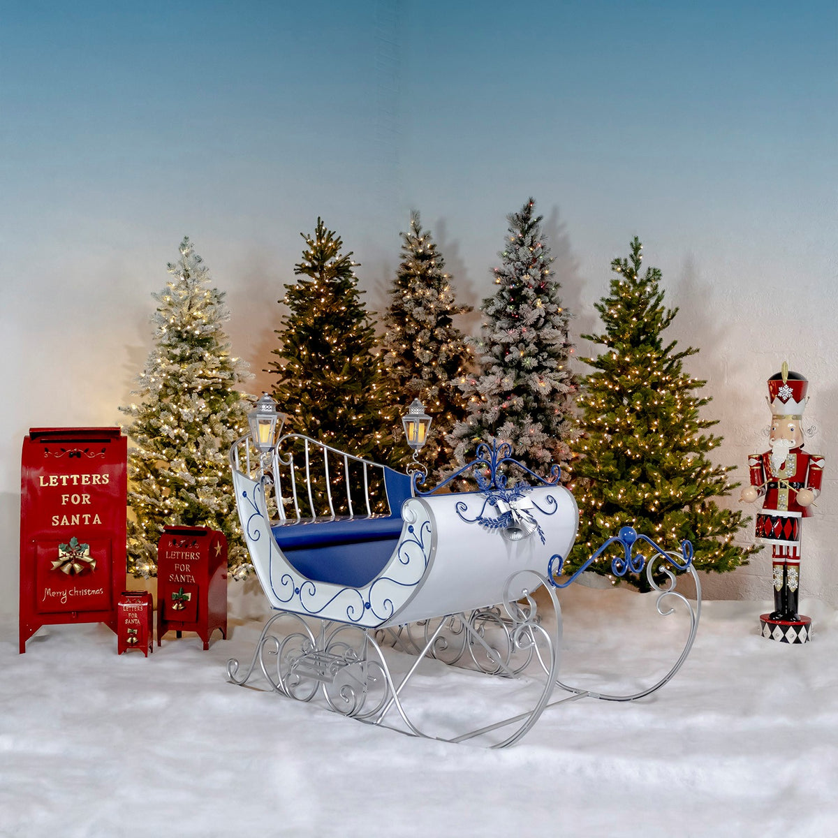 Large Victorian style iron Christmas sleigh in glossy snow white with royal blue and silver trim, two silver lanterns, and a royal blue seat