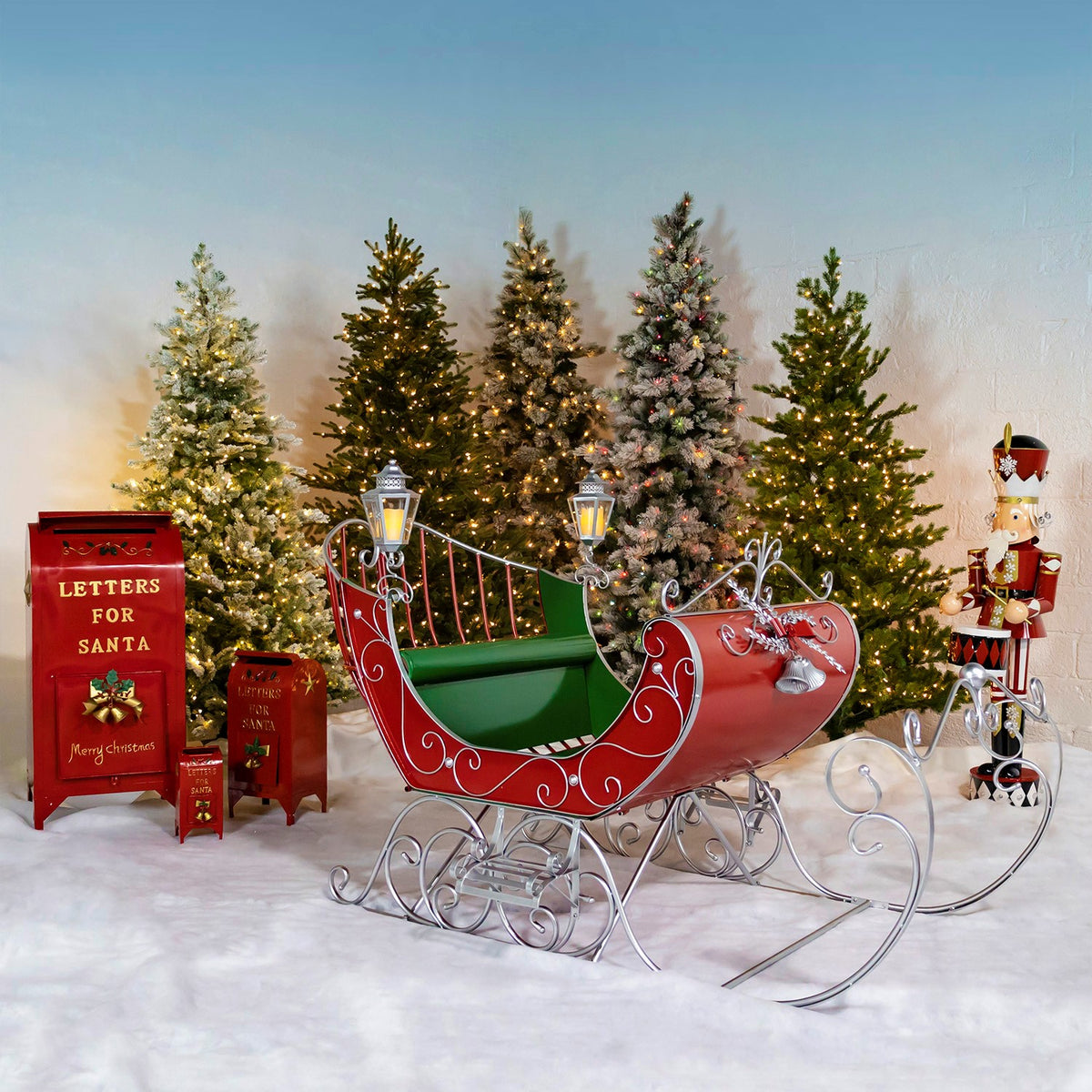 Large Victorian style iron Christmas sleigh in glossy red with green and silver trim, two silver lanterns, and a royal blue seat