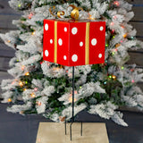Red iron Christmas gift box yard stake with white polka dots and a metallic gold ribbon and bow