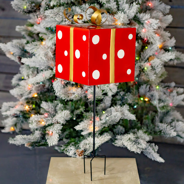 Red iron Christmas gift box yard stake with white polka dots and a metallic gold ribbon and bow