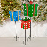 Three iron Christmas gift box yard stakes in red, green, and blue with white stars and bows