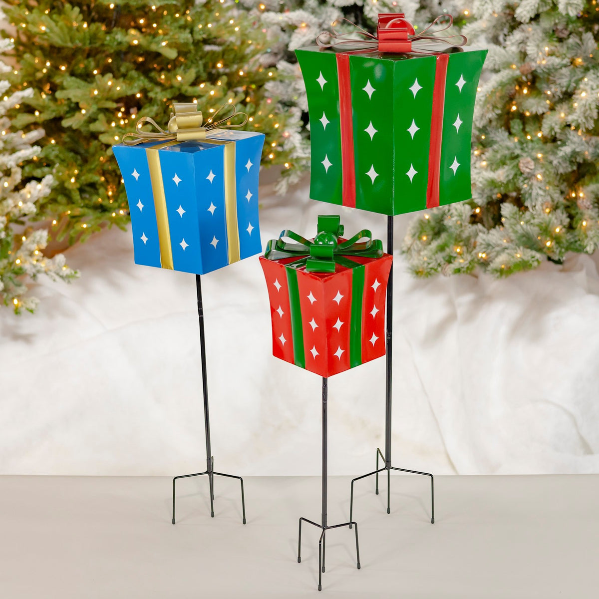 Three iron Christmas gift box yard stakes in red, green, and blue with white stars and bows