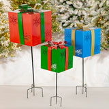 Three iron Christmas gift box yard stakes with snowflake cutouts in red, blue, and green with metal bows
