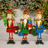 Set of three hand painted metal nutcracker figurines in red, blue, and green holding a tree, wreath, and gifts