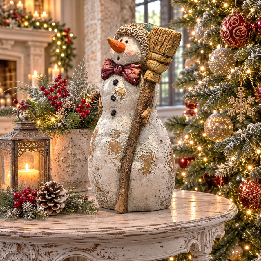 Vintage-style polyresin snowman figurine with a rustic broom, knit cap, and scarf in a distressed hand painted finish