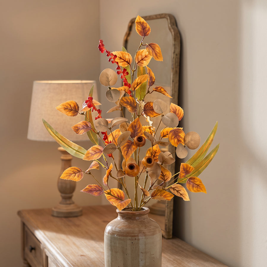 Fall foliage sprays in a ceramic vase on a console in a warm autumn living room