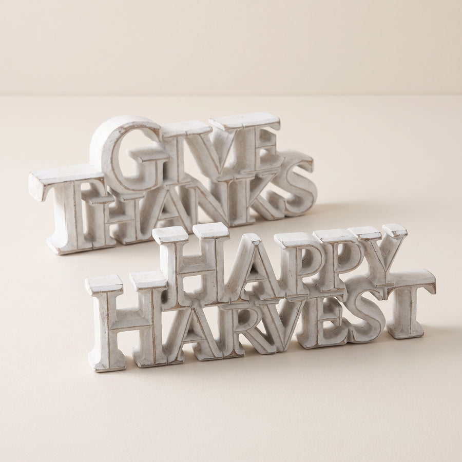 Two white-washed resin tabletop signs reading happy harvest and give thanks in two sizes, raised studio angle on a plain surface