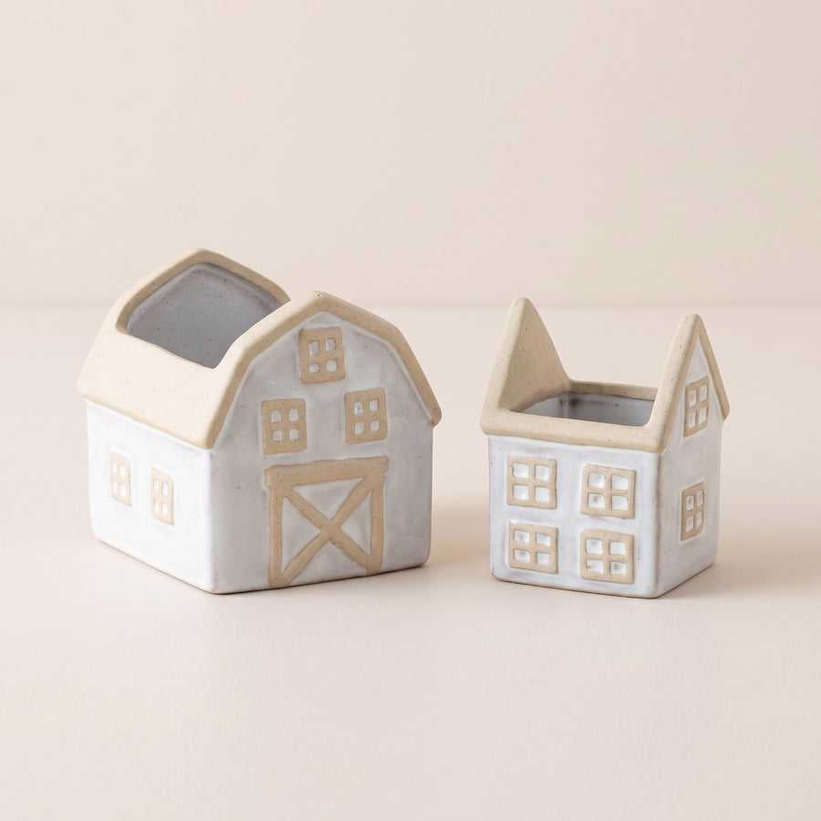 Two beige and white porcelain planters shaped like a house and a barn in two sizes, raised studio angle on a plain surface