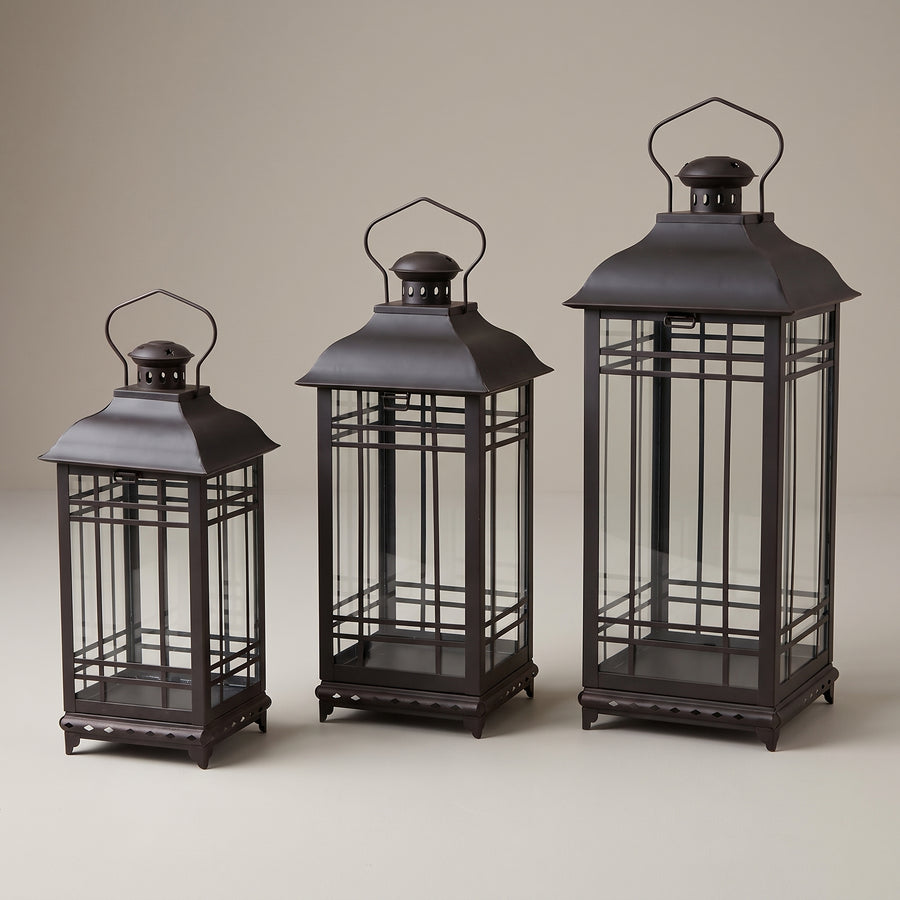 Three black metal and glass lanterns in graduated heights of fourteen, seventeen and twenty inches, raised studio angle on a plain surface