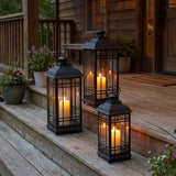 Three graduated black lanterns with glowing candles on covered porch steps at dusk