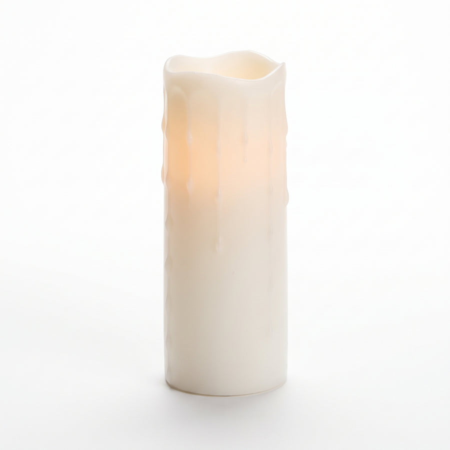 Macro of a very tall white LED pillar candle showing long streaming wax drips and a warm glow from inside the column
