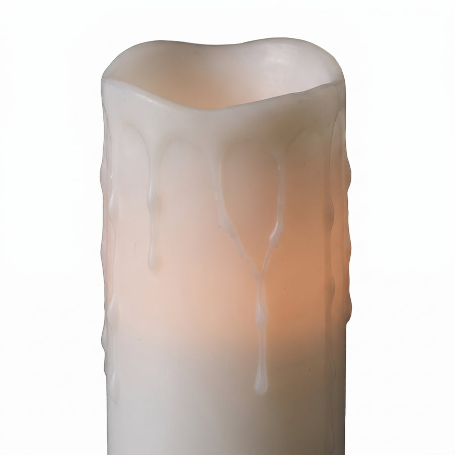 Macro of a tall white LED pillar candle showing long wax drips and a warm glow from inside the column