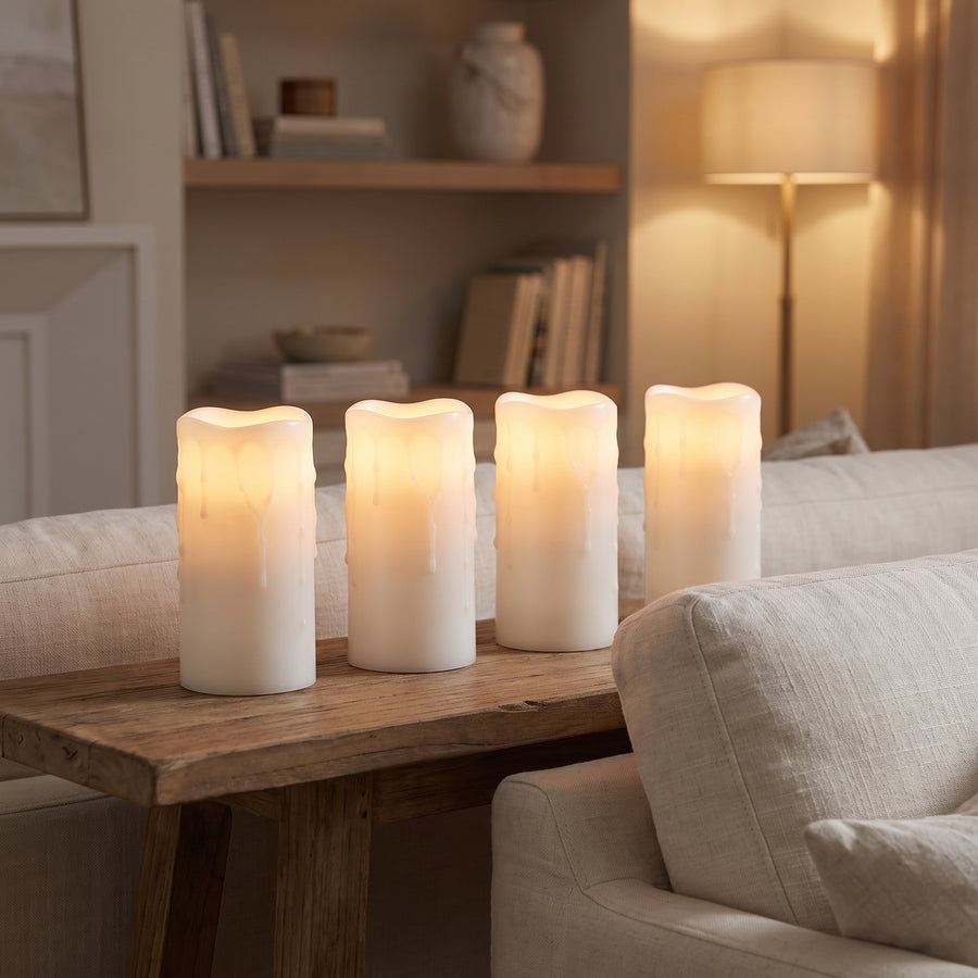Four tall flameless pillar candles glowing on a console behind a sofa in a calm evening living room