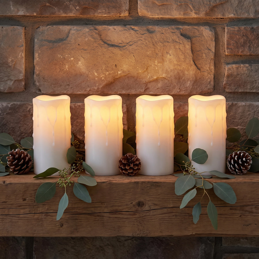 Four tall glowing white pillar candles staggered on a mantel at dusk with pinecones and eucalyptus