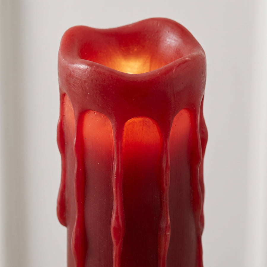 Macro of a tall red LED pillar candle showing deep red wax drips and a warm glow from inside the column