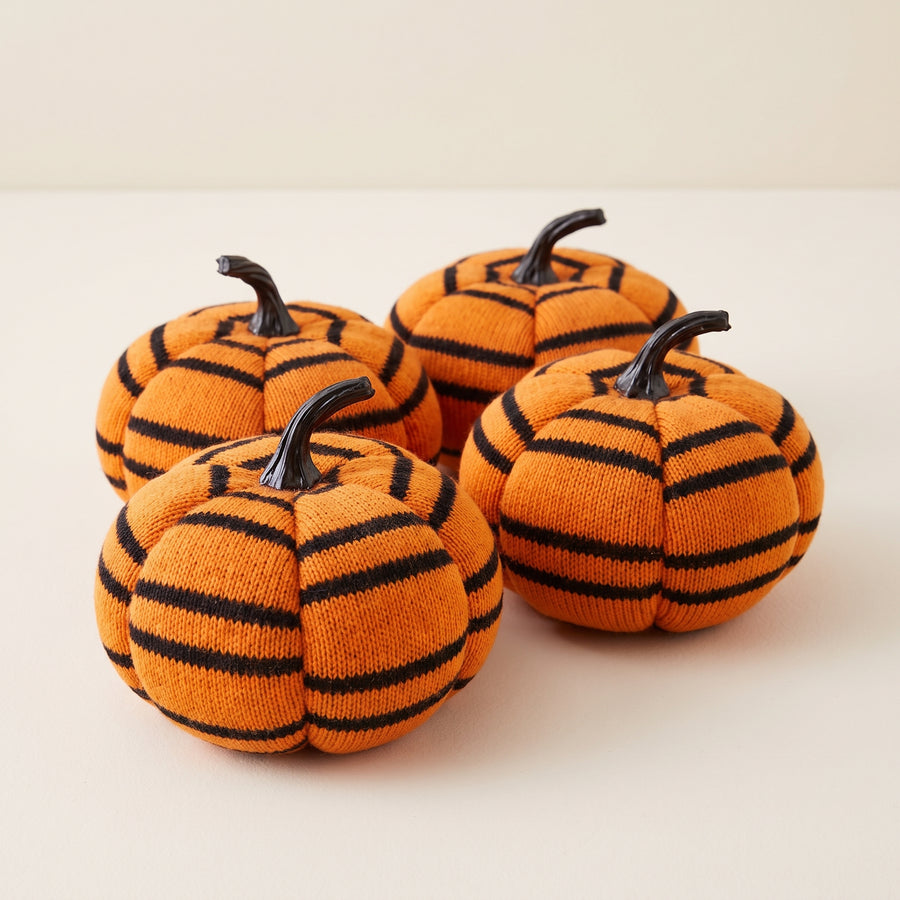 Four plush pumpkins with orange and black vertical stripes, about five inches each, raised studio angle on a plain surface