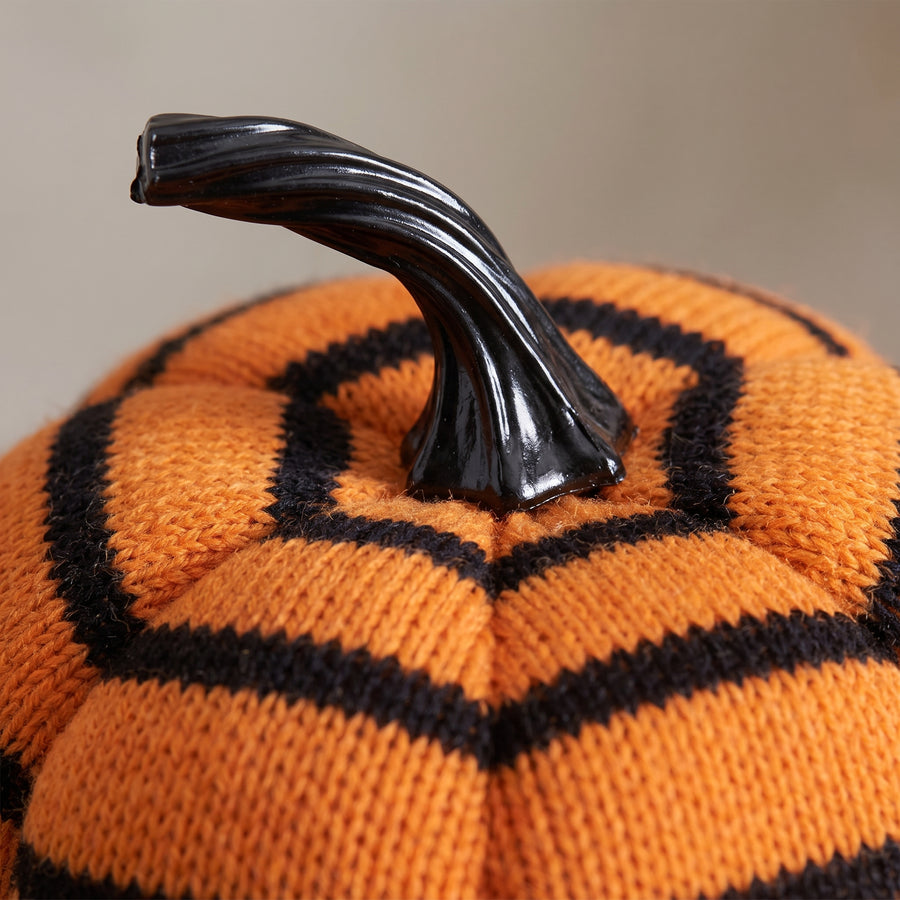 Macro of a plush striped pumpkin showing knitted orange and black ribs and a glossy black moulded resin stem