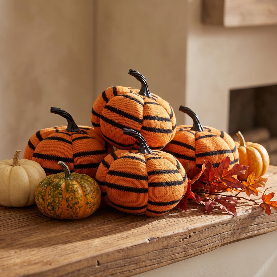Four orange and black striped plush pumpkins clustered on a fall mantel with mini gourds