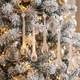 Clear glittered teardrop icicle sprays hanging on a white flocked Christmas tree