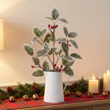 Frosted holly and red berry sprays in a tall white enamel pitcher on a wooden console with a plaid runner and candles