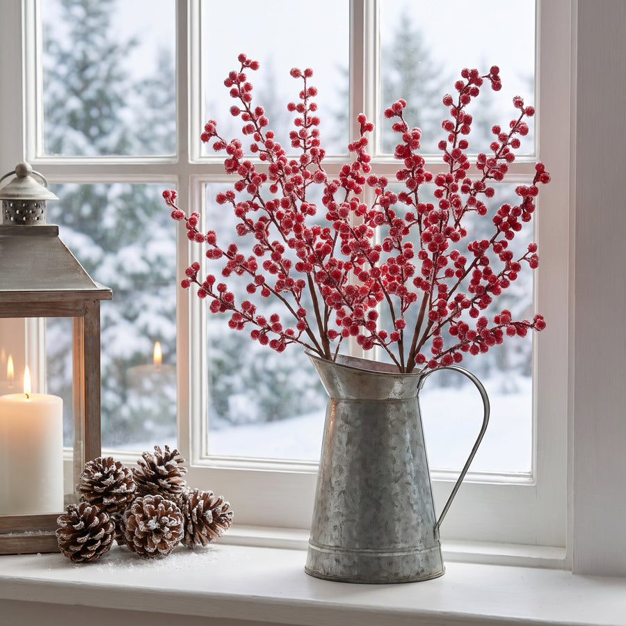 Iced red berry twig sprays in a galvanized pitcher on a snowy winter windowsill