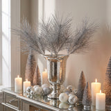 Silver glittered pine sprays in a mercury glass urn on a mirrored Christmas console