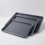 BLACK+DECKER 3-piece carbon steel baking sheet set with ceramic nonstick coating in 13, 15 and 17 inch sizes on a studio surface