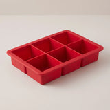 Red silicone ice cube tray with six large square wells for slow-melting cocktail cubes, Houdini, on a studio surface