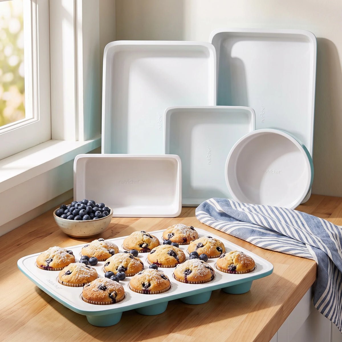 NutriChef turquoise and white nonstick bakeware set on a counter with a muffin pan of fresh blueberry muffins
