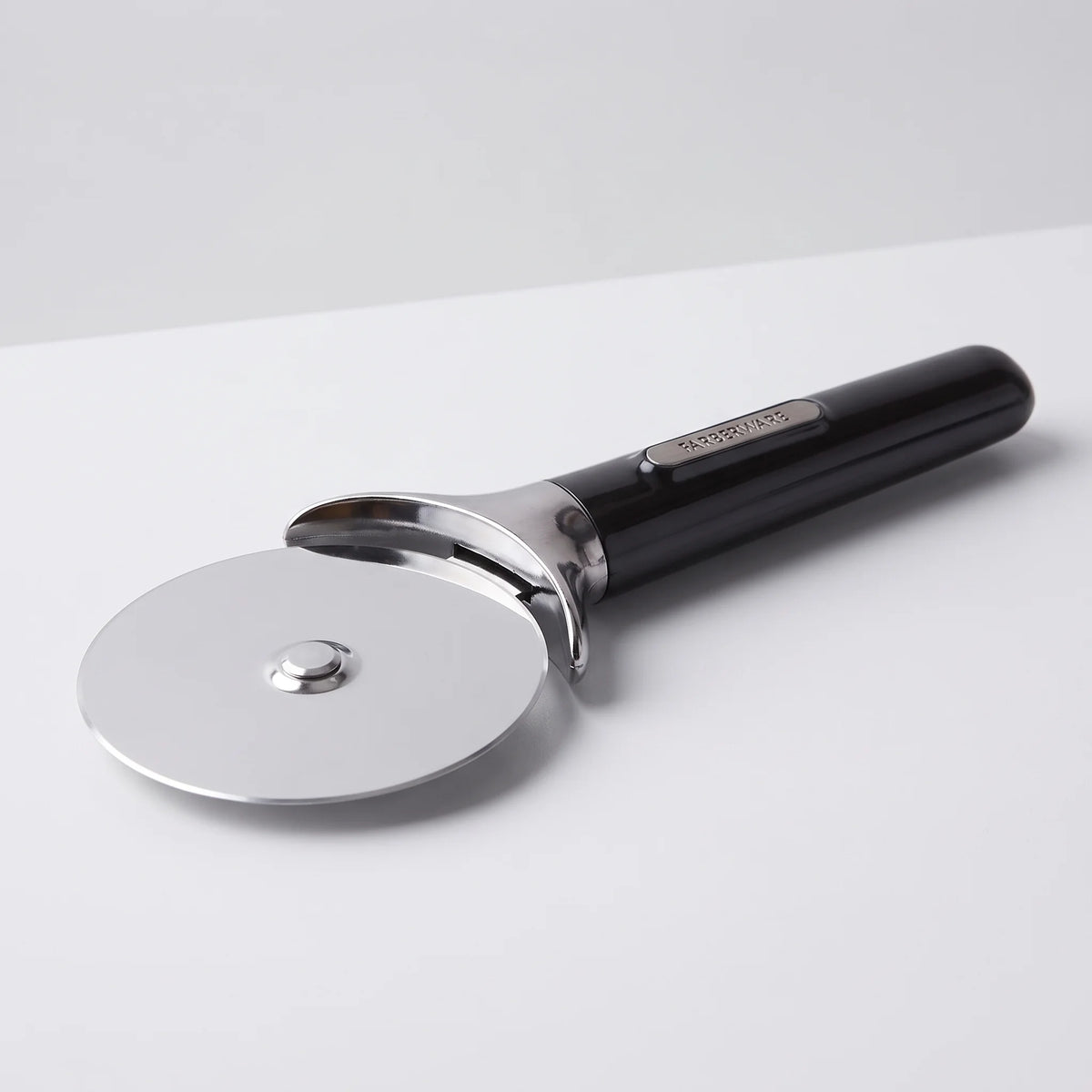 Farberware professional stainless steel pizza cutter wheel with black comfort grip handle and finger guard on a studio surface