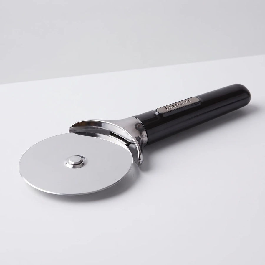 Farberware professional stainless steel pizza cutter wheel with black comfort grip handle and finger guard on a studio surface
