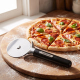 Farberware stainless steel pizza cutter on a wood board beside a freshly sliced pepperoni pizza