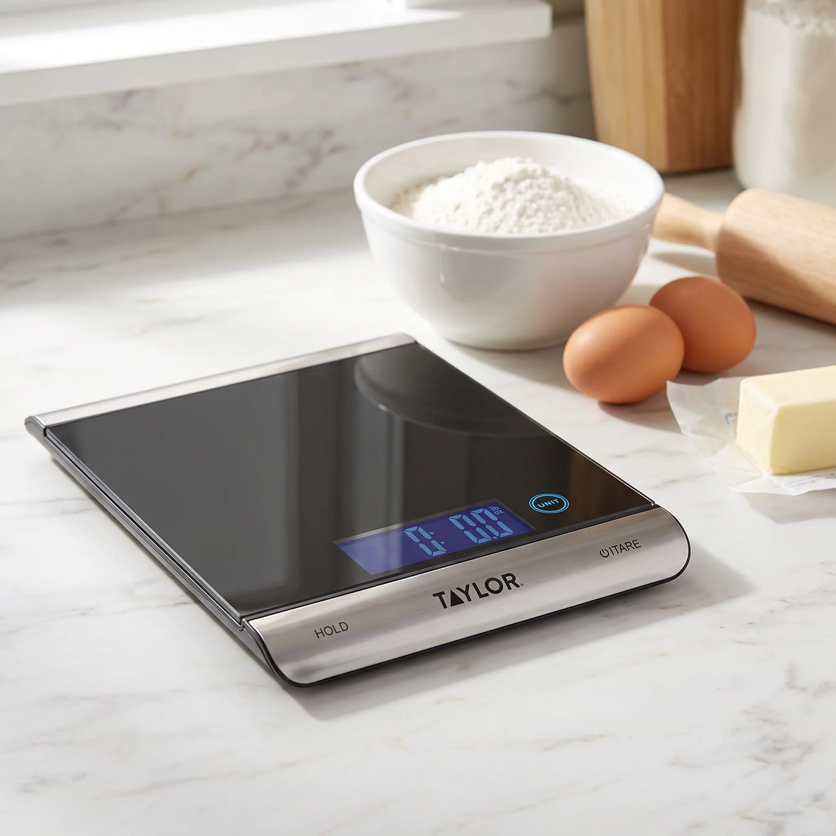 Taylor 3851 digital kitchen scale on a marble baking counter beside flour, eggs and butter