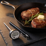 Taylor digital instant read thermometer on a slate board beside seared steaks in a cast iron skillet