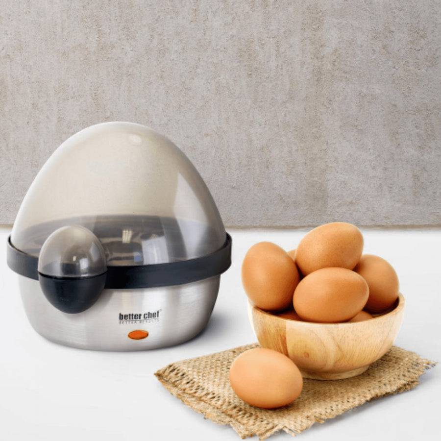 Better Chef stainless steel electric egg cooker with a see-through lid next to a wooden bowl of brown eggs