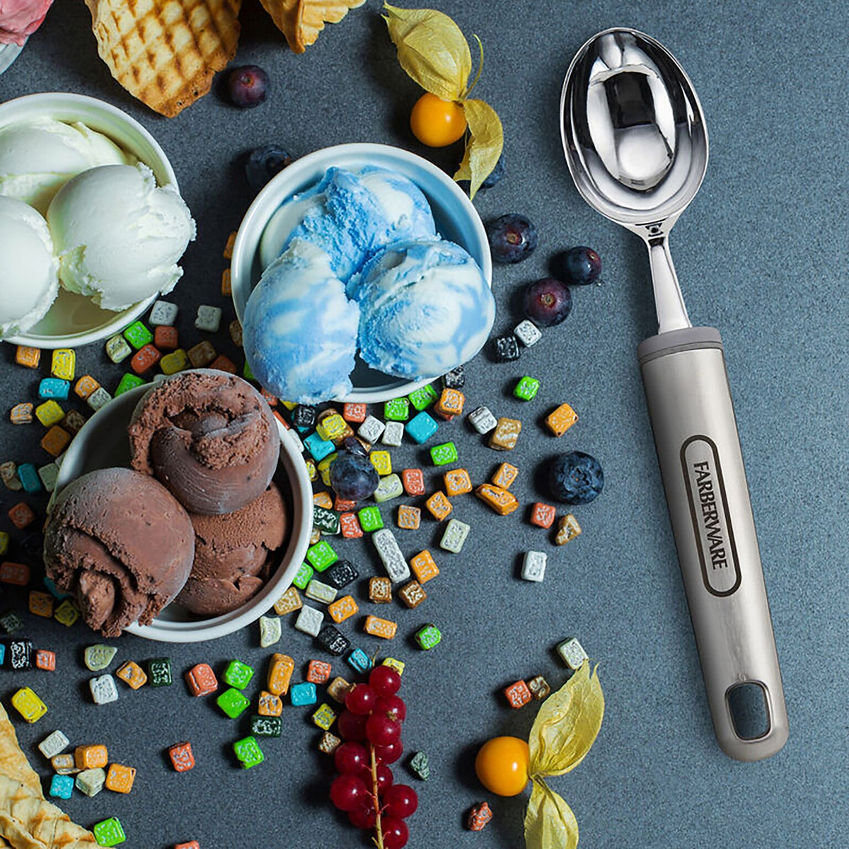Farberware soft ice cream scoop with a scoop of ice cream beside bowls of mixed ice cream flavors
